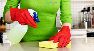 Woman with bottle of cleaning fluid and sponge cleaning benchtop